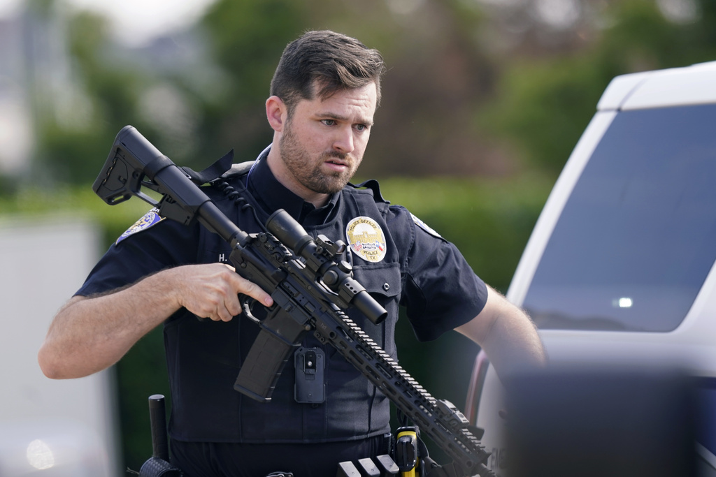 A law enforcement officer carries a rifle as people are evacuated from a shopping center 