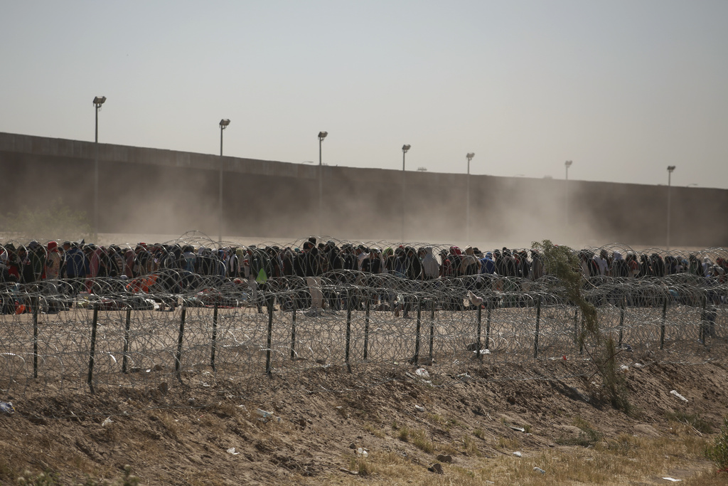 Migrants line-up between a barbed-wire barrier and the border fence at the US-Mexico border, as seen from Ciudad Juarez, Mexico