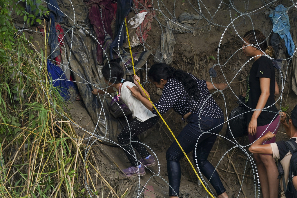 Migrants walk through a barbed-wire barrier into the United States after crossing the Rio Bravo from Matamoros, Mexico