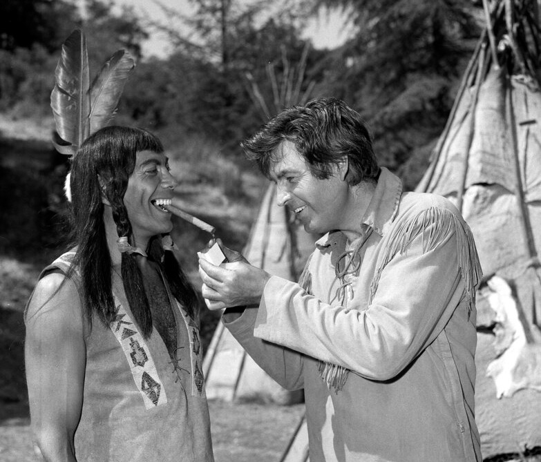 Fess Parker (r), star of the NBC-TV "Daniel Boone" show, lights the cigar of singer-actor Ed Ames (l), Oct. 23, 1964. Parker was passing out cigars between takes on the set, celebrating the birth of a daughter
