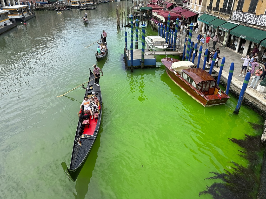 A bright patch of green is seen in the Grand Canal along an embankment lined with restaurants, in Venice, Italy, Sunday, May 28, 2023. Police in Venice are investigating the source of a phosphorescent green liquid patch that appeared Sunday in the city's famed Grand Canal.