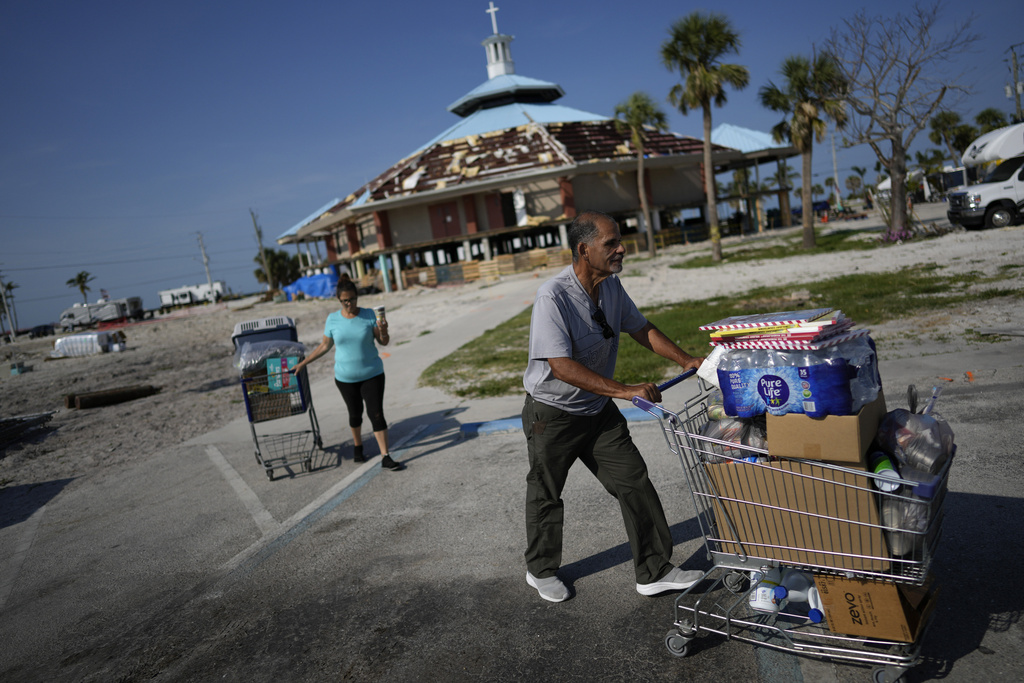 Omar Del Rio and his wife Maria wheel shopping carts full of groceries and supplies to their car as they leave the free food pantry operating underneath the heavily damaged Beach Baptist Church in Fort Myers Beach, Fla.