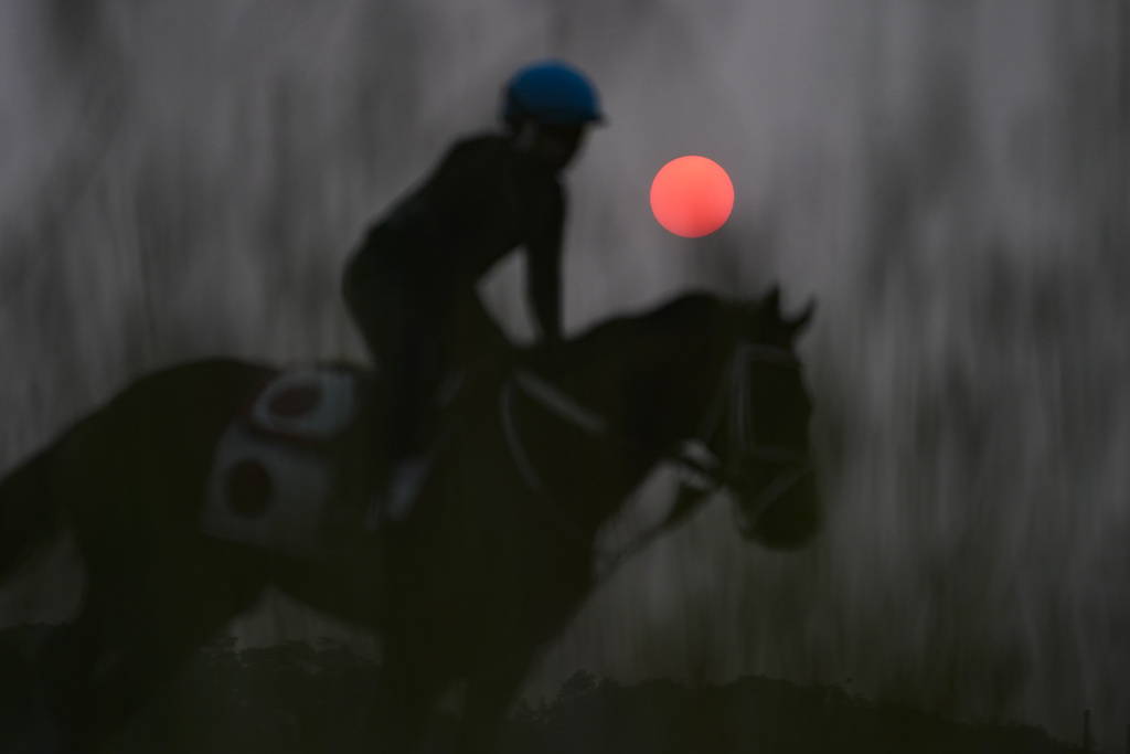Haze from northern wildfires obscures the rising sun as horses train ahead of the Belmont Stakes horse race at Belmont Park in Elmont, N.Y.
