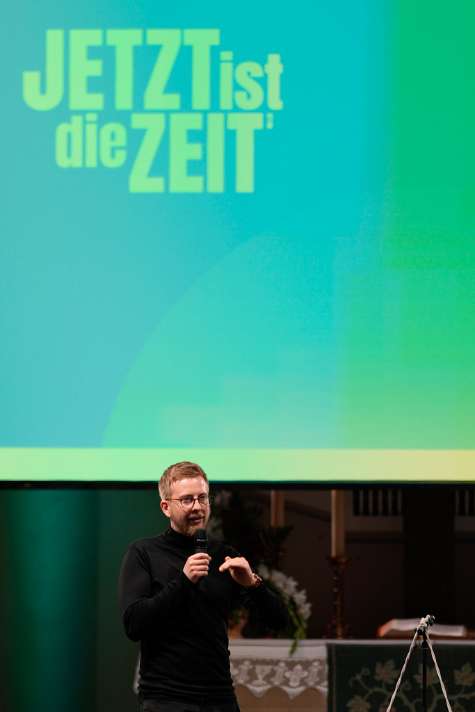 Jonas Simmerlein, theologian and philosopher from the University of Vienna in Austria, gestures in front of a slogan reading 