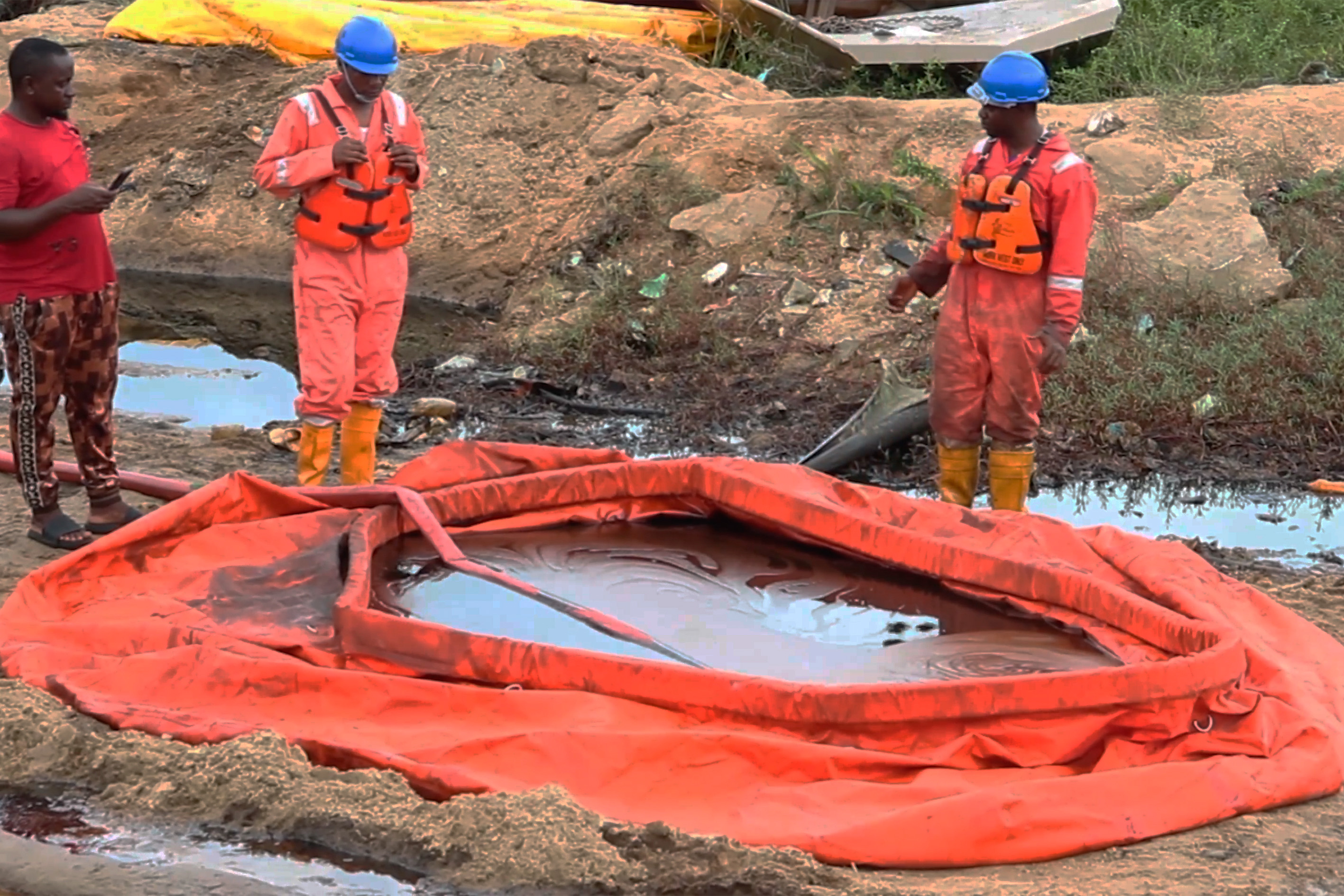 Three workers stand around an orange balloon with trapped oil-filled water inside