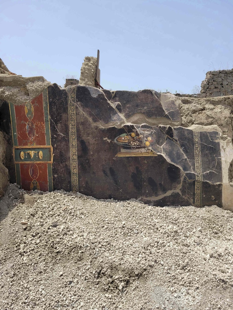 The wall of an ancient Pompeian house with frescoes, one depicting a table with food