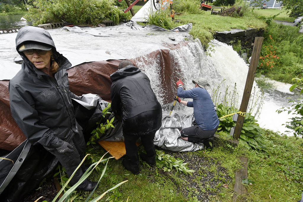 Meg Dawkins, left, and other community members, use tarps to keep the Curtis Pond dam from getting undermined