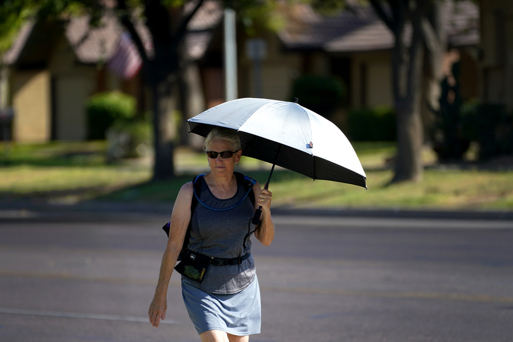 A lady uses an umbrella for shade to combat high temperatures, Monday, July 10, 2023 in Phoenix