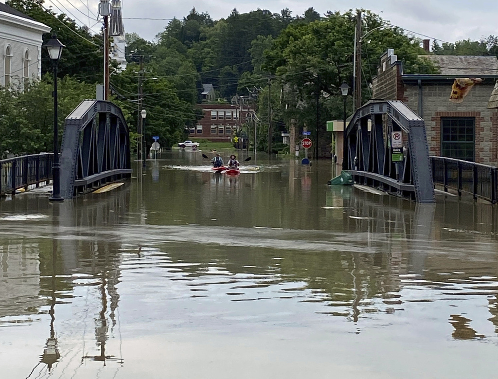 2 kayakers paddle through floodwaters as they approach the School Street Bridge in Montpelier, Vt.