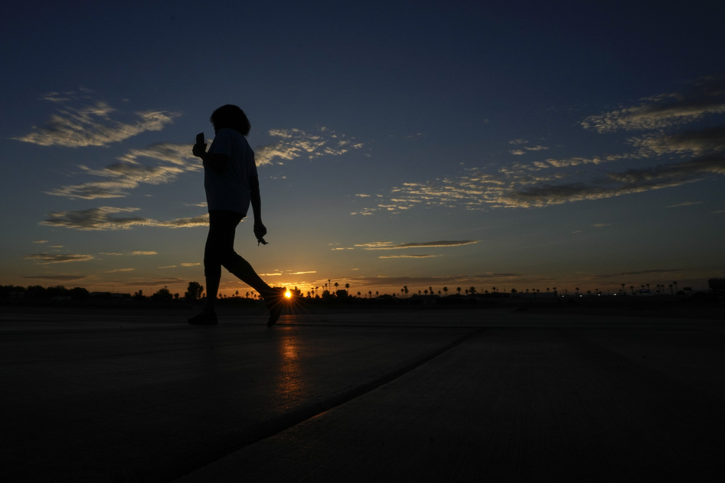 Janice Edwards listens to a podcast on her phone as she walks at sunrise Tuesday, July 11, 2023, in Yuma, Ariz.