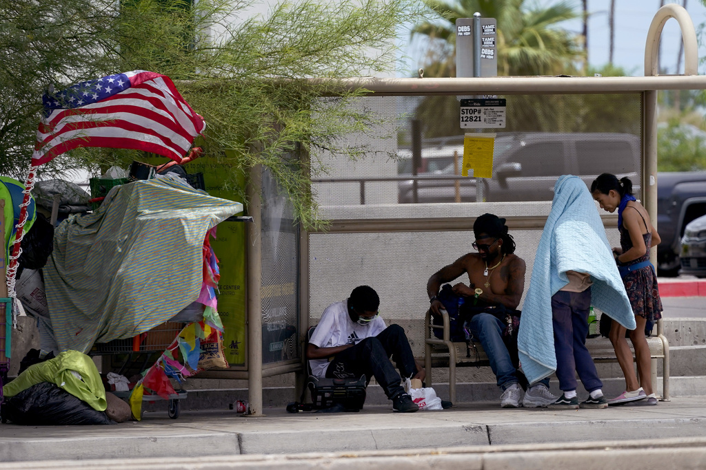 People gather under the shade of a bus stop, Tuesday, July 11, 2023 in Phoenix. Even desert residents accustomed to scorching summers are feeling the grip of an extreme heat wave smacking the Southwest.