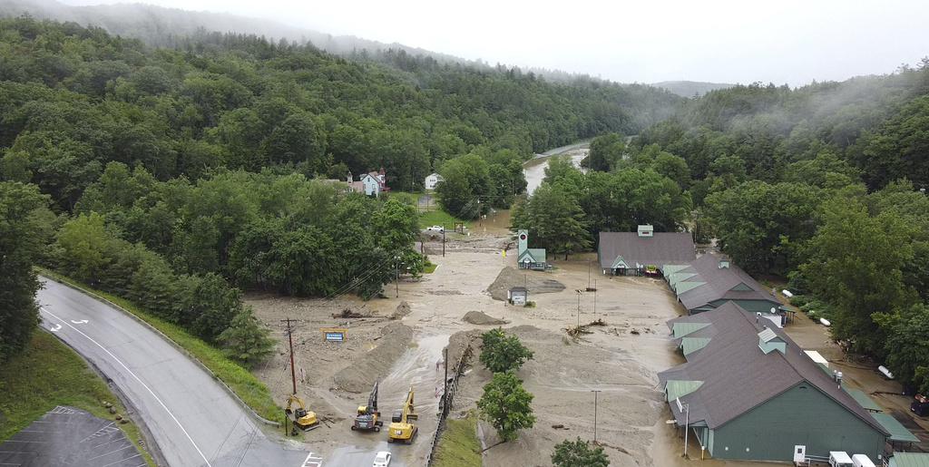 construction vehicles stand by as muck, mud and floodwater block a section of Route 203 in Ludlow, Vt.