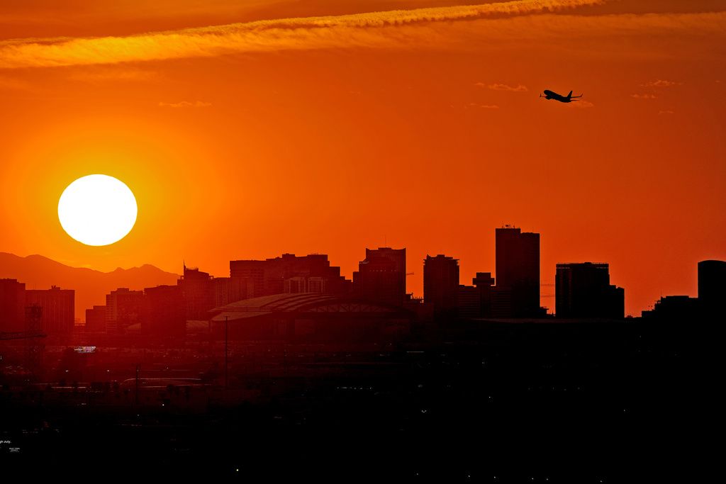 A jet takes flight from Sky Harbor International Airport as the sun sets over downtown Phoenix