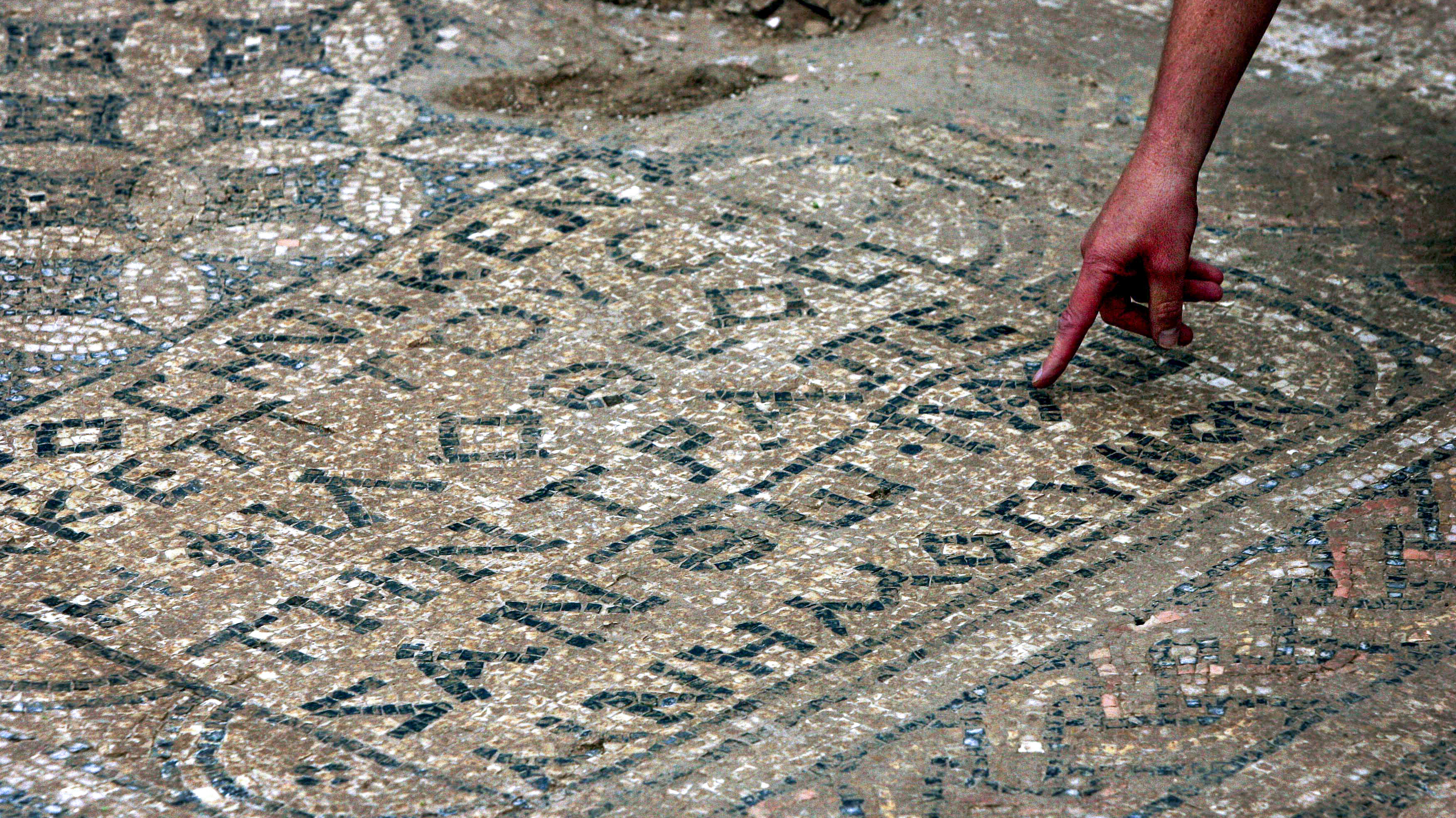 Man pointing to ancient Greek text written in the mosaic