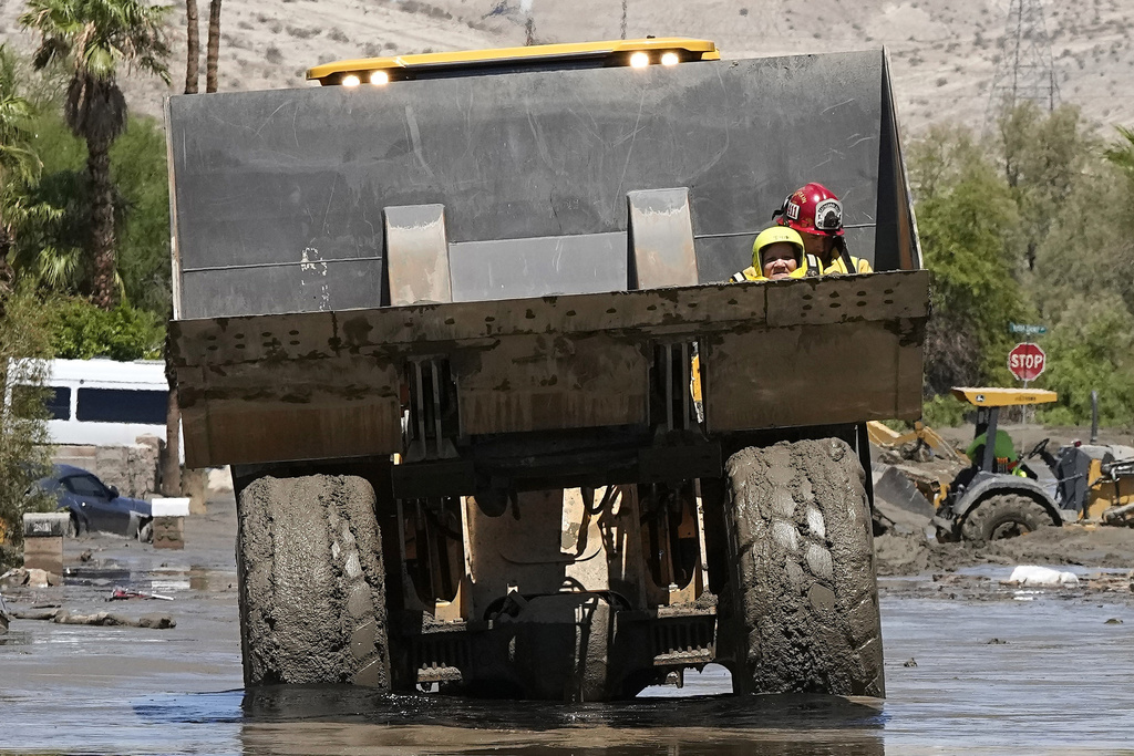 Firefighters use a skip loader to rescue a person from an assisted living center after the street was flooded with mud