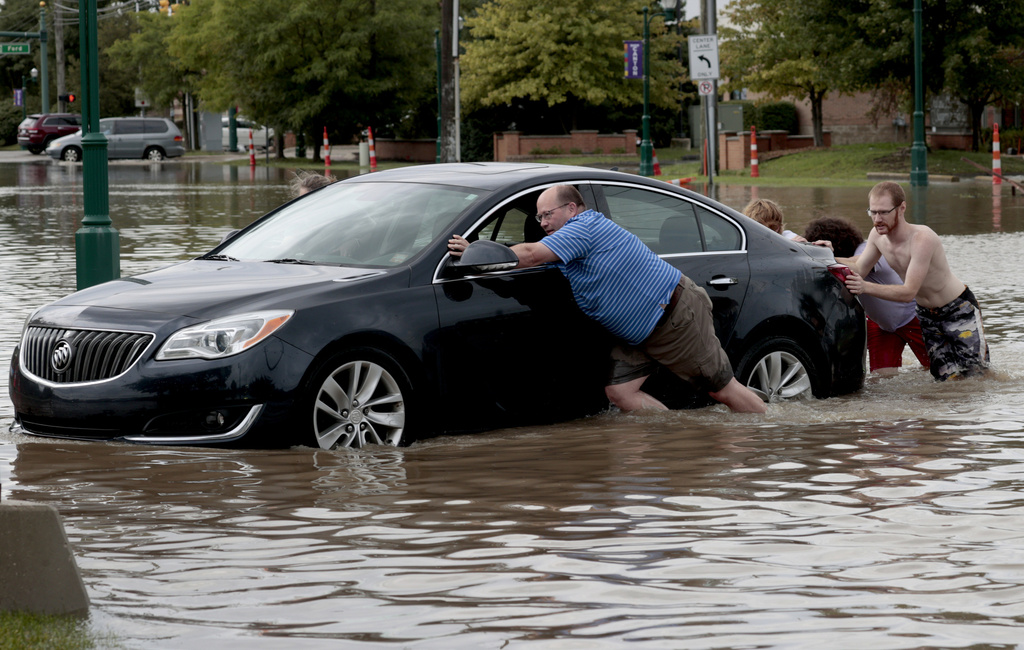 People help push a car out of floodwaters after a woman got stuck in the middle of Canton Center Road in Canton, Mich