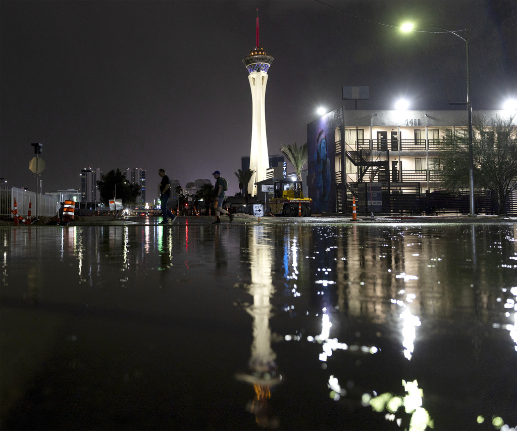 Two men walk past floodwaters after thunderstorms on Wednesday, Aug. 23, 2023, in Las Vegas