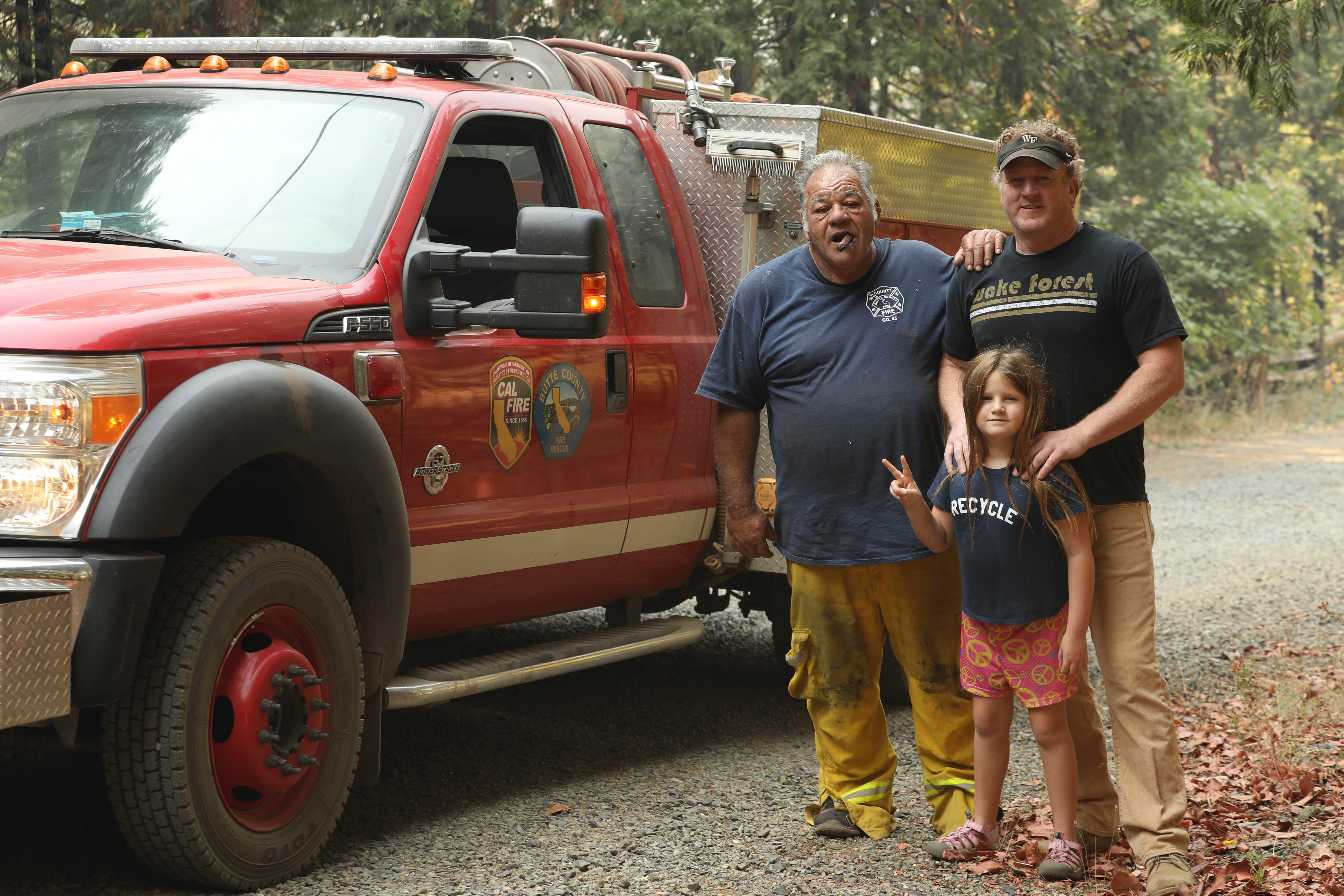 Firefighter, man and daughter next to fire truck in the woods