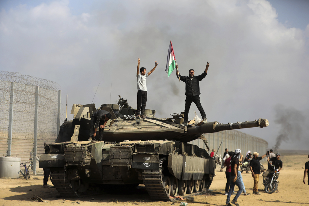 Palestinians wave their national flag and celebrate by a destroyed Israeli tank at the Gaza Strip fence east of Khan Younis