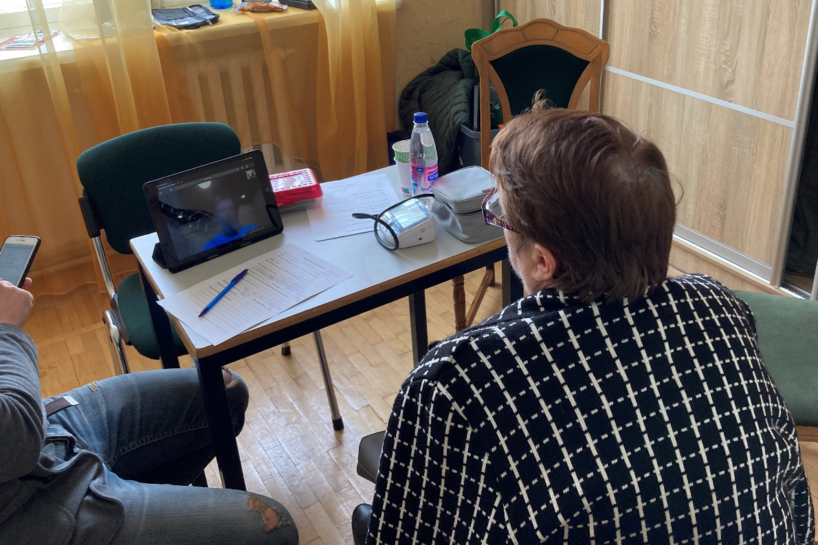 The person at the desk is the patient consulting. The (blurred) face on the screen is the healthcare provider in another country. You can see the telemedicine equipment sitting around on the desk, the exam is over and they are in the discussion phase of the visit.