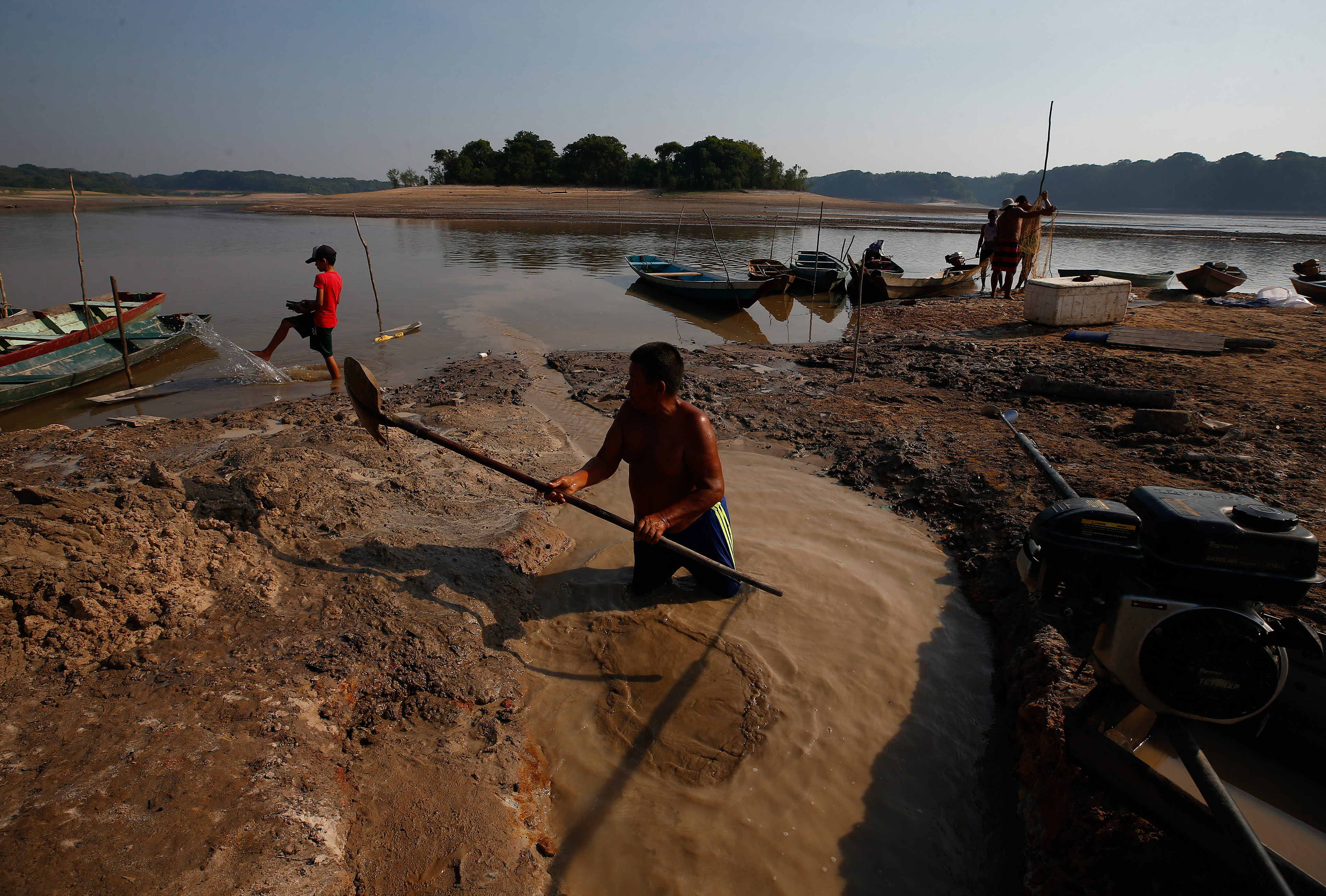 Man shoveling through mud to find water with a boy in the background.