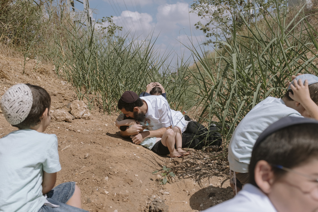 Israelis take cover as a siren sounds a warning of incoming rockets fired from the Gaza Strip in Rehovot, Israel