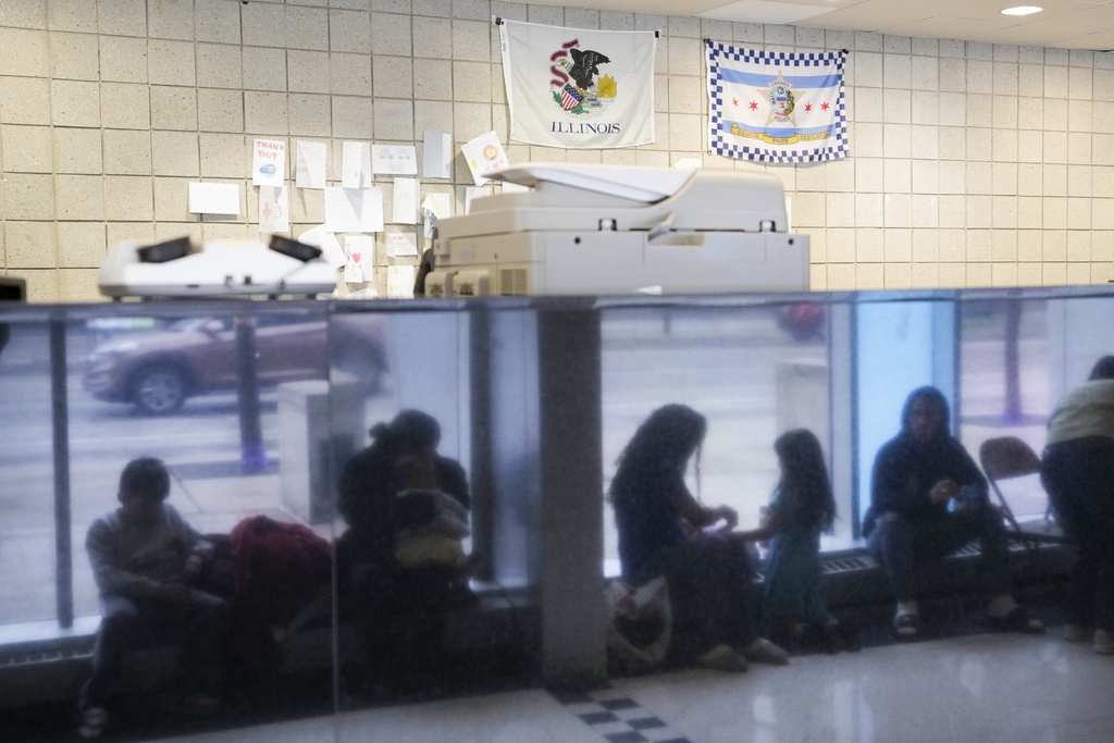 Immigrants from Venezuela are reflected in a marble wall while taking shelter at the Chicago Police Department