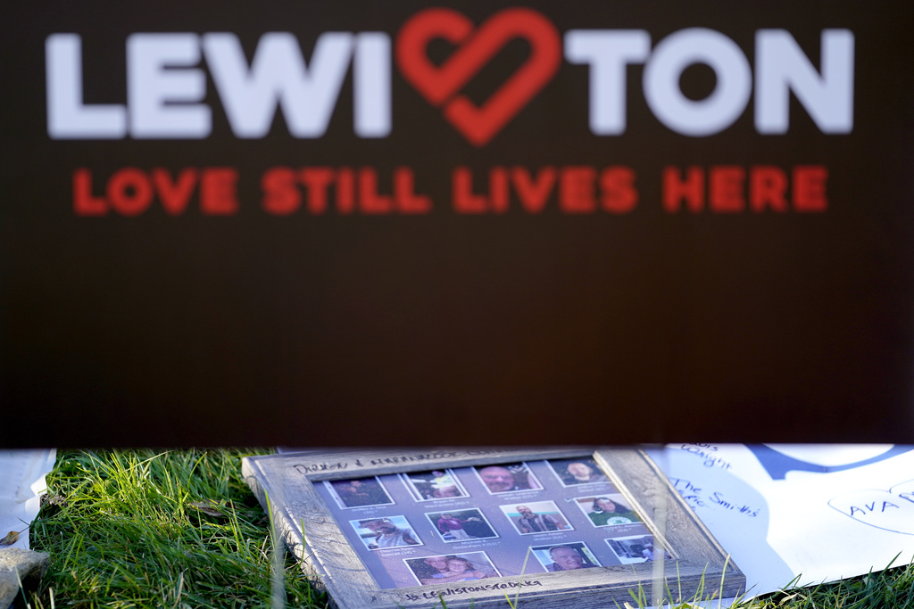 Photographs of the Lewiston shooting victims rest under a sign at a memorial outside Schemengees Bar & Grille