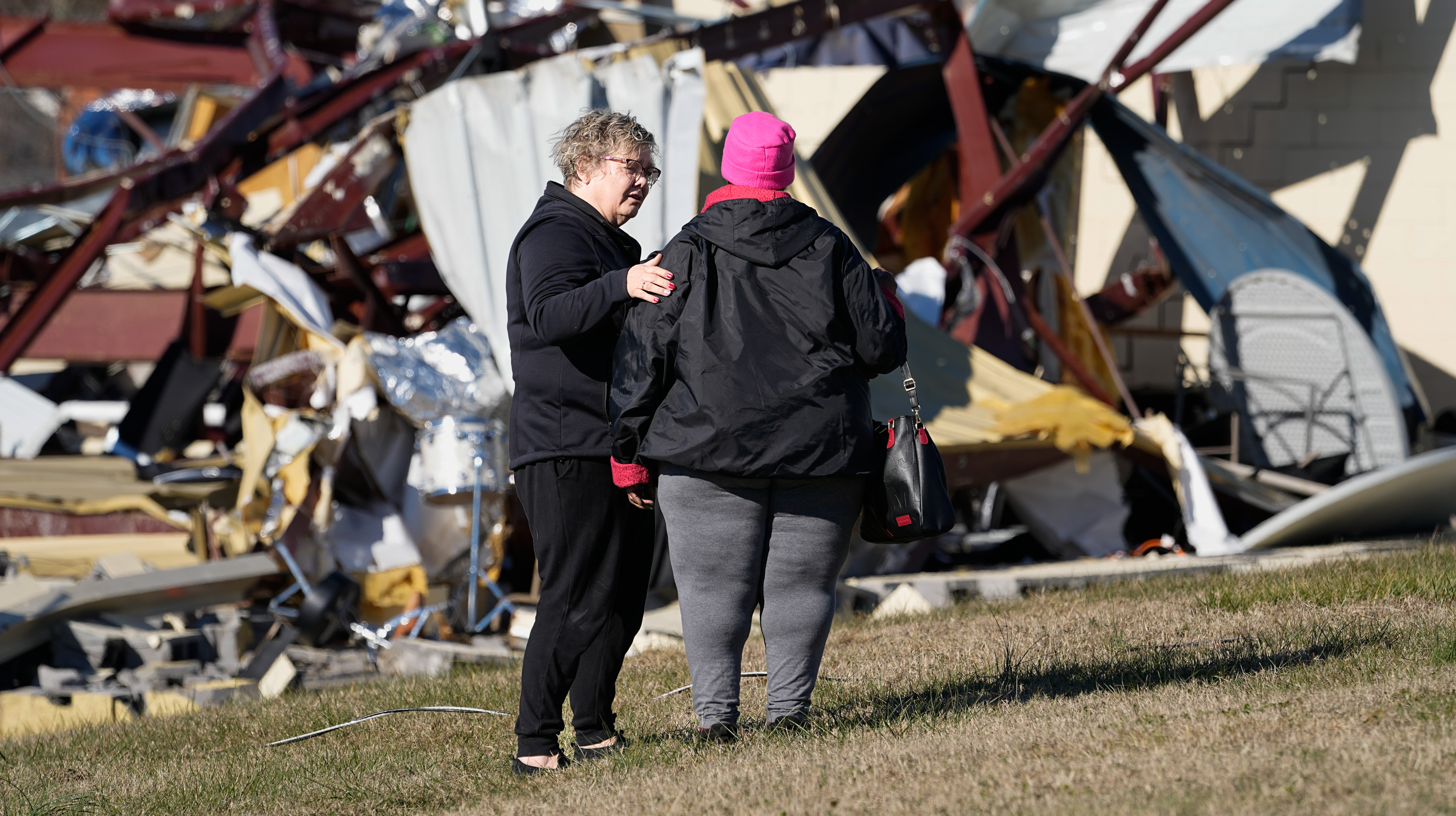 A woman comforting another woman outside of a damaged church.