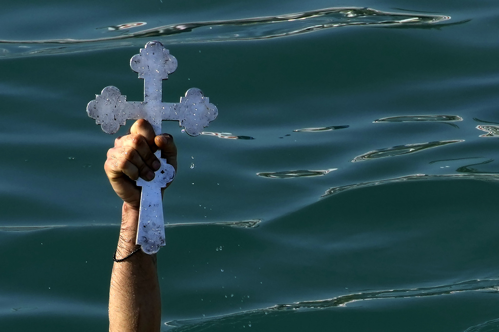 A pilgrim holds up the cross after it was thrown into the water by an Orthodox priest, during an Epiphany ceremony to bless the sea, on the southeast resort of Ayia Napa, Cyprus