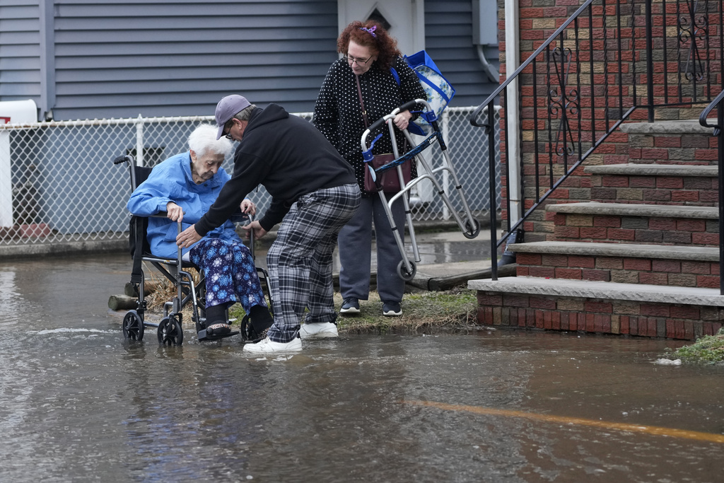 People help a woman in wheelchair through a flooded street in Lodi, N.J.
