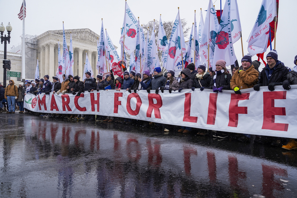 People holding the March for Life banner pause as they march past the Supreme Court