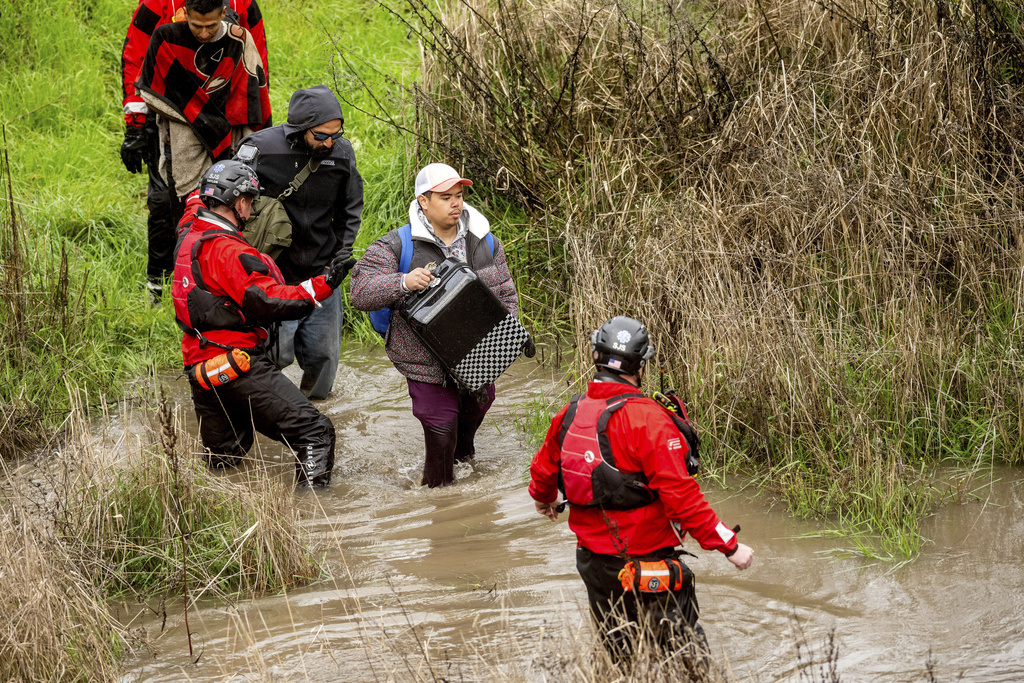 Search and rescue workers evacuate men from a homeless encampment that became surrounded by floodwater from the Guadalupe River in San Jose, Calif.