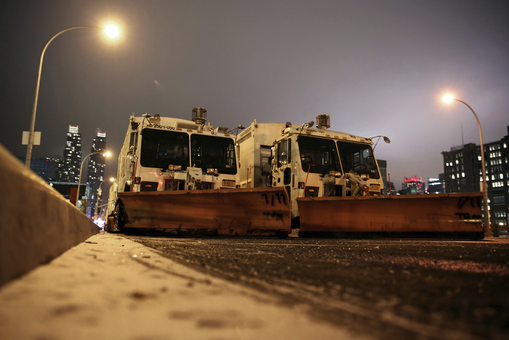 Sanitation trucks mounted with snow plows are parked on the west side of Manhattan in New York