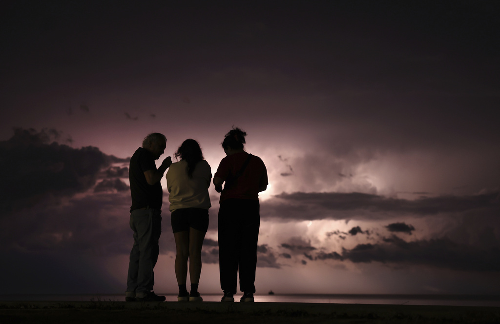 Armando Perez, left, and Gabby Perez, right flank their niece, Victoria Perez, as they watch lightning illuminating the sky at Montrose Harbor as a storm moves over the Lake Michigan following two days unseasonably warm weather