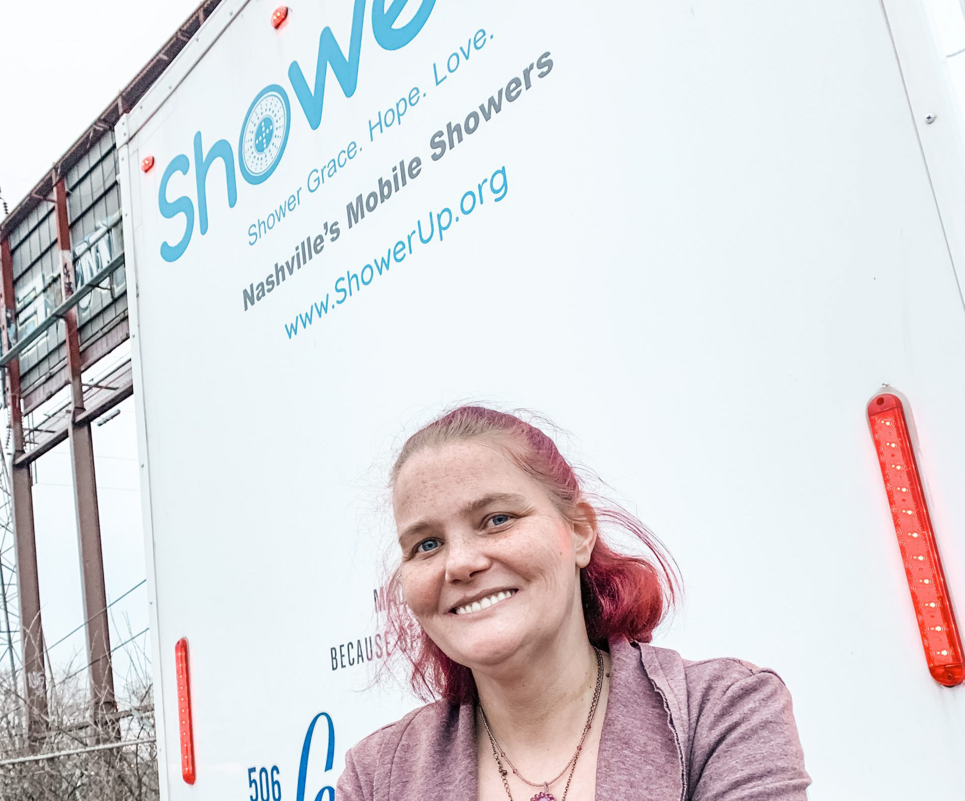 Woman smiling in front of Nashville Shower Up mobile shower unit