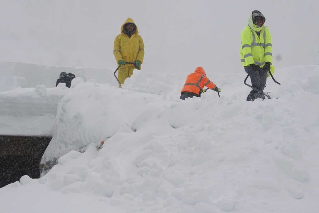 Workers clear snow off a roof of a building