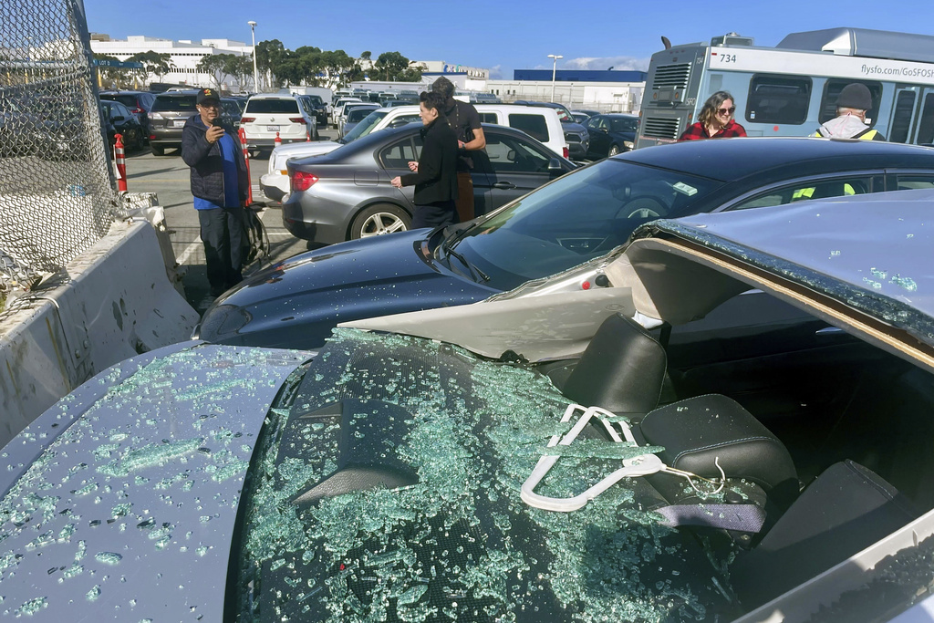 People view damaged cars in an on-airport employee parking lot after tire debris from a Boeing 777 landed on them at San Francisco International Airport