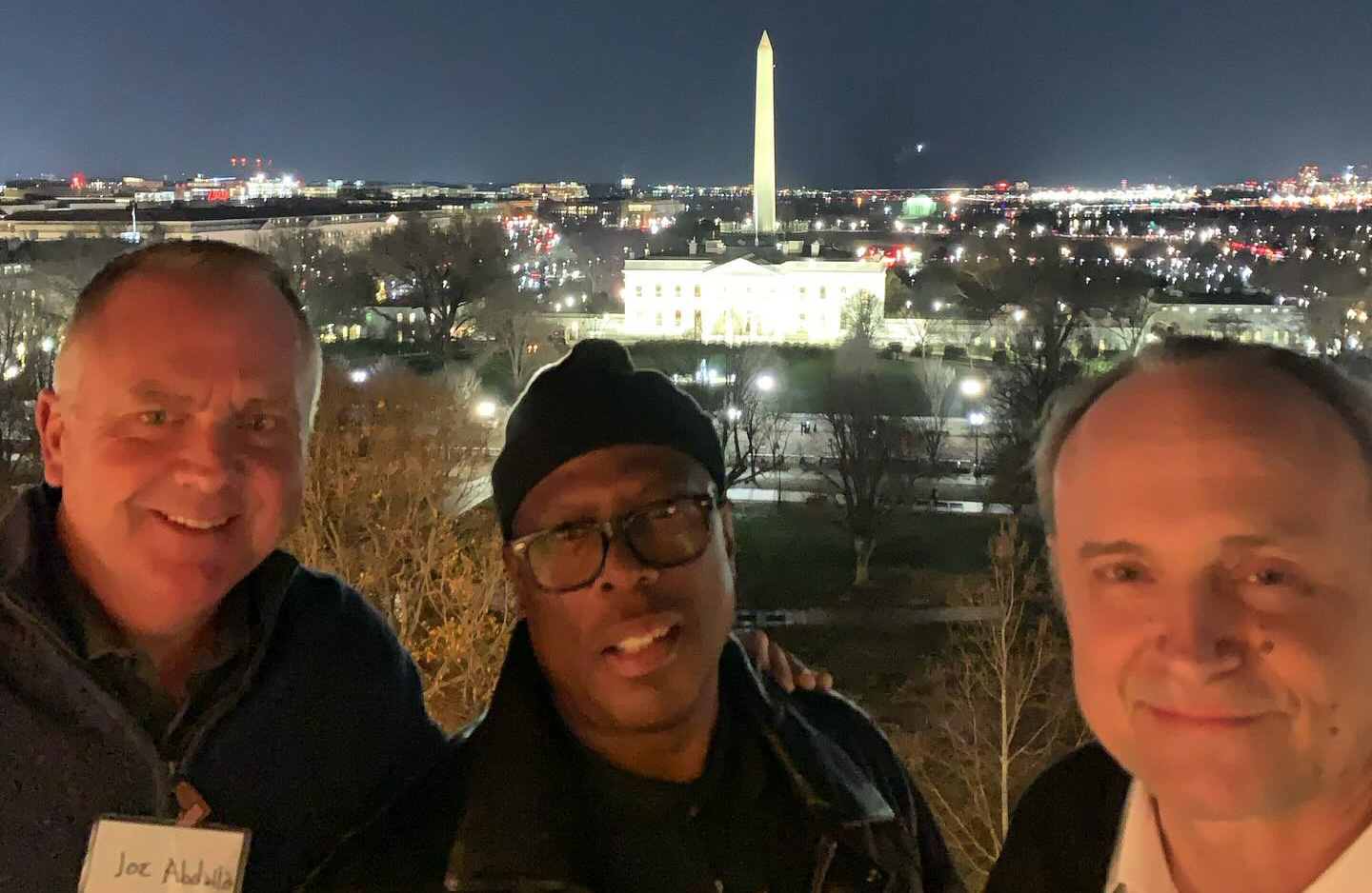 Three men standing in the foreground of the Washington Monument and The White House