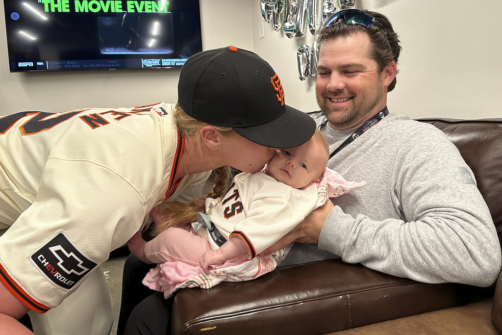 San Francisco Giants major league assistant coach Alyssa Nakken, left, kisses her daughter, Austyn, as her husband, Robert, watches before a baseball game between the Giants and the San Diego Padres