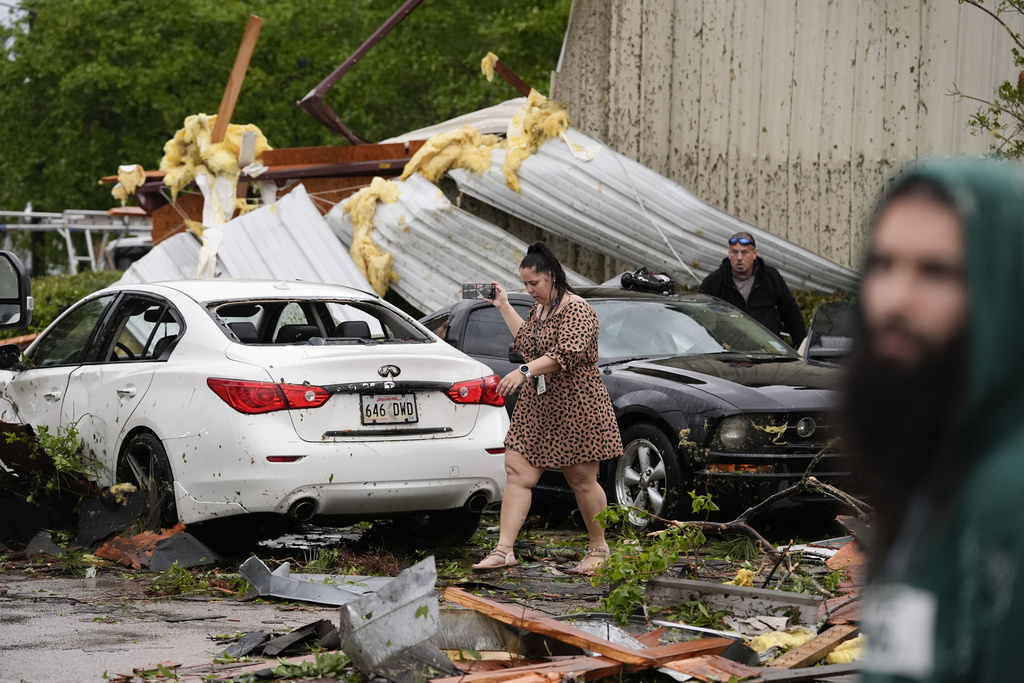 Woman walks past heavily damaged car following severe storm