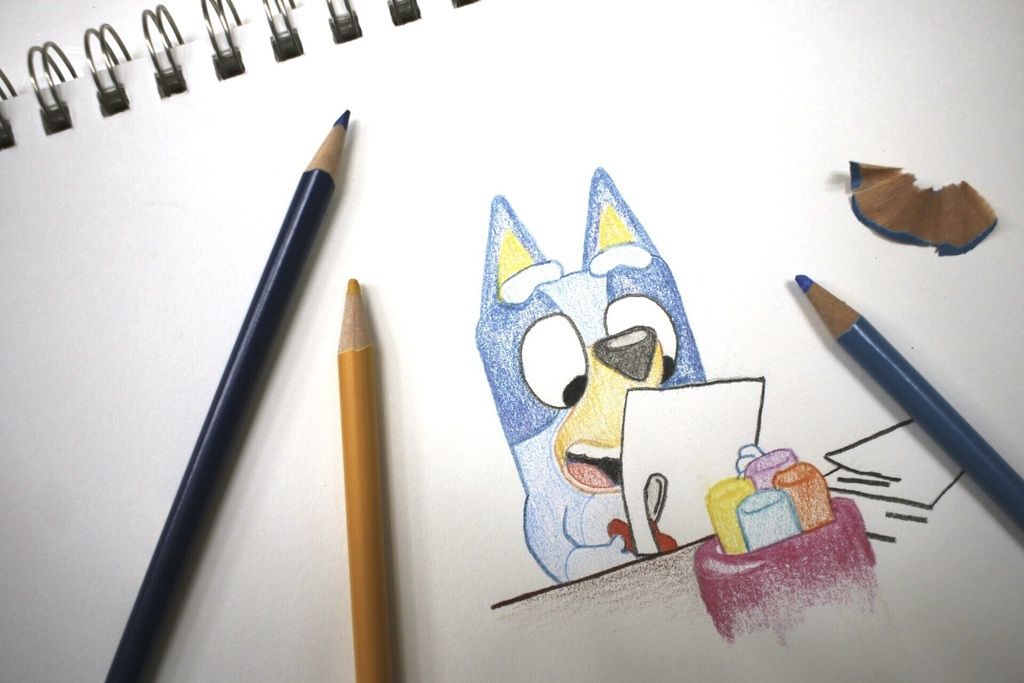 Colored pencils sit around a drawing of "Bluey" the Australian kids
