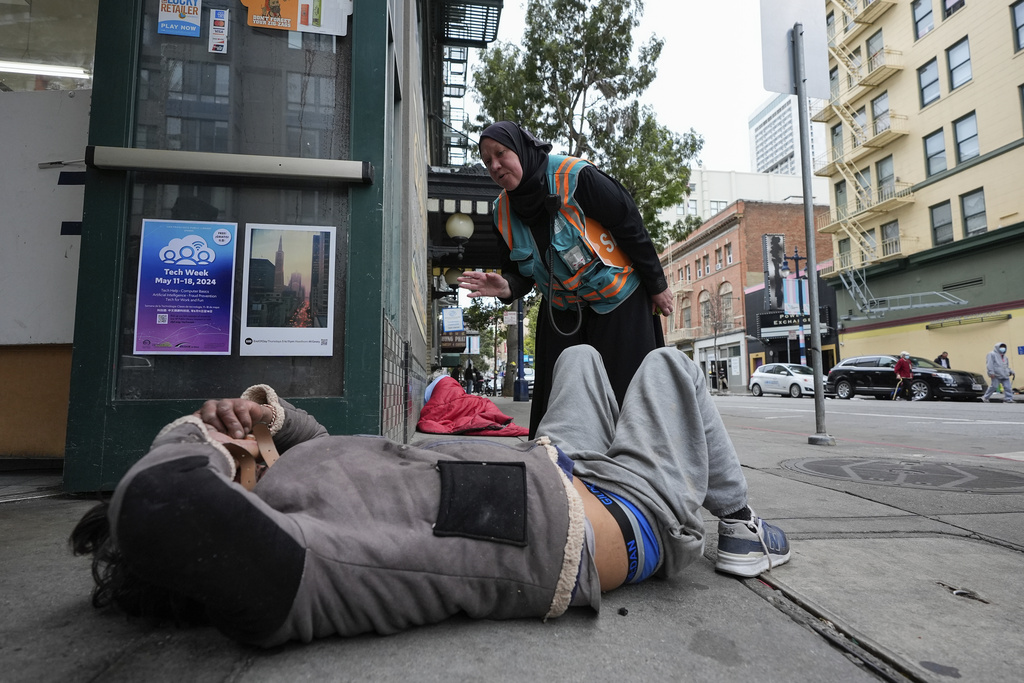 Tatiana Alabsi, right, checks on a man laying on a sidewalk and asks him to please move before children start walking to school in the Tenderloin neighborhood