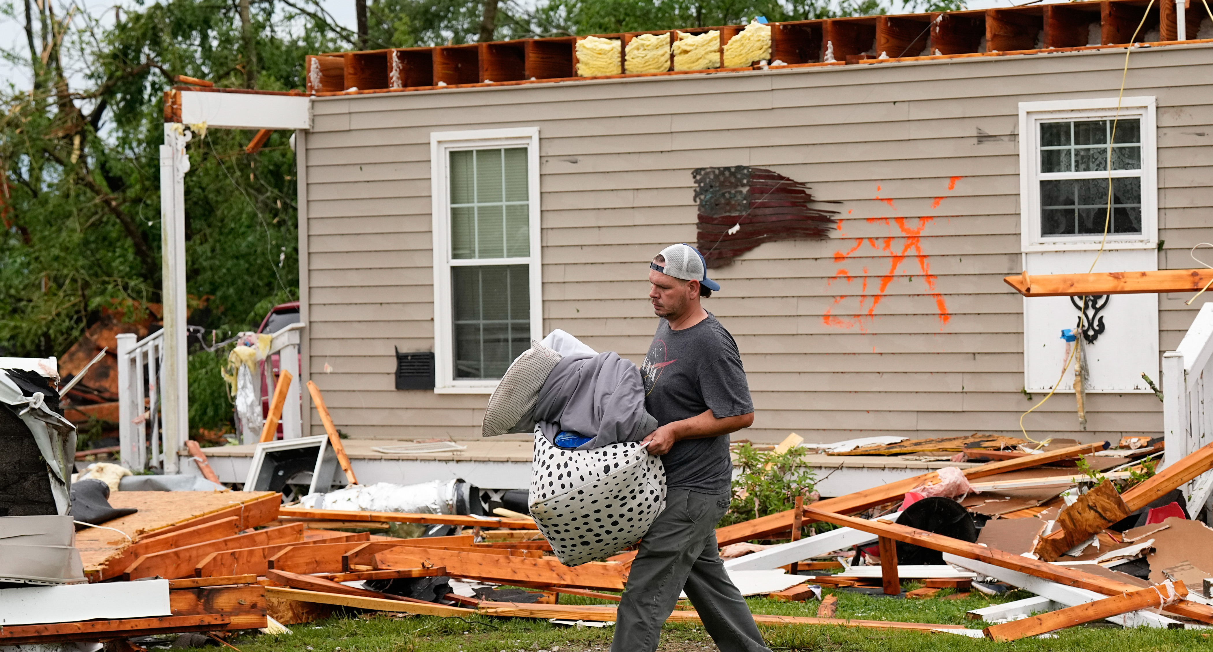 Man removing belongings from tornado-ravaged home.