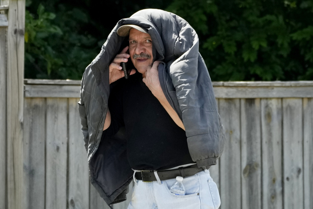 Man talks on the phone as he covers his head with his jacket during hot weather in Glenview, Ill.