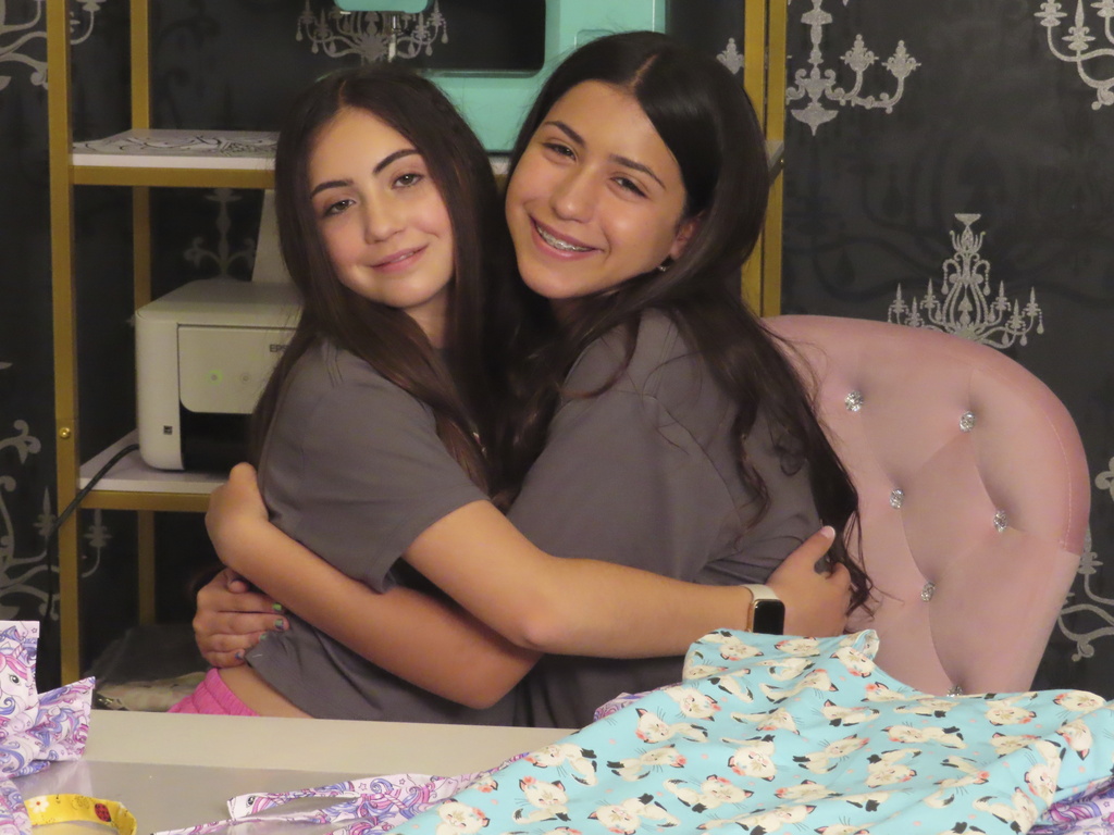 Audrina Demma, left, and her sister Giuliana hug in the basement at the sewing station of their Freehold, N.J.