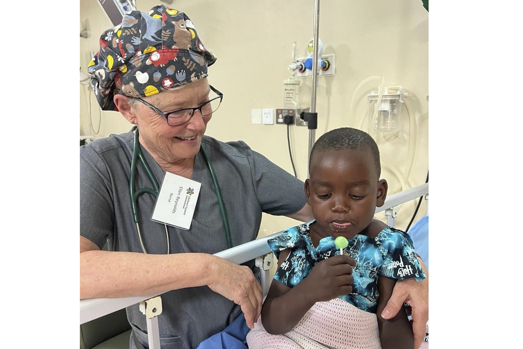 Nurse Ellen Reynolds of Children’s Surgery International gives a lollipop to patient Ategeka, whose last name they are keeping confidential to protect his privacy, in a bed at Holy Innocents Children