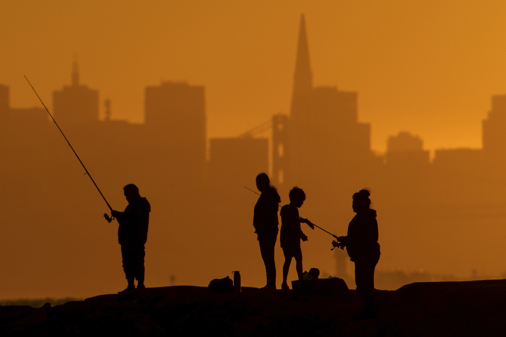 With the San Francisco skyline behind them, people fish off a jetty in Alameda, Calif. 