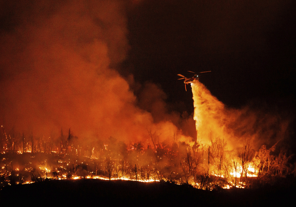 A night flying helicopter drops water on flames as the Thompson Fire burns