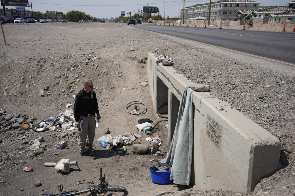 Mark Paulson, a Public Response and Code Enforcement officer, holds cans of cold water while checking on a homeless encampment